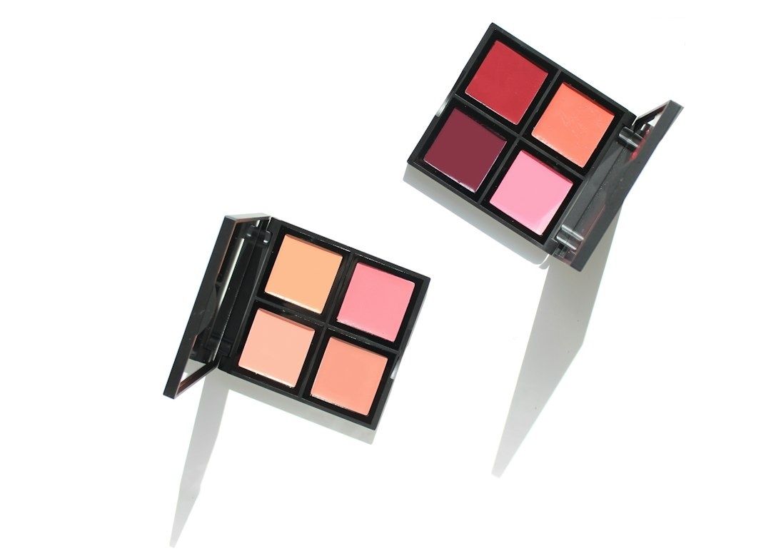Två öppna paletter med färgkorrigerande makeup i rosa och persikotoner